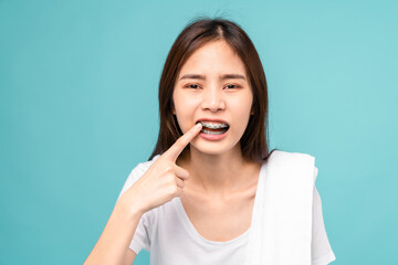 Woman wearing braces with sensitive teeth and hands touch the cheeks on blue background, Concept oral hygiene and health care.