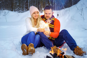 Happy couple man and woman hugging in winter in the forest by the fire with sparklers