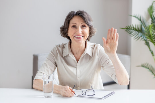 Head shot portrait caucasian aged businesswoman makes video call looks at camera and smiling, happy senior leader shows gesture of greeting employee at online meeting, hiring by video conference