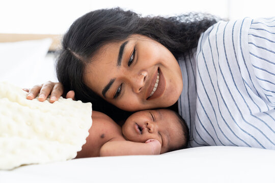African American mum kissing her newborn baby on the bed. Closeup of infant with mother. Woman and adorable little African American baby on bed