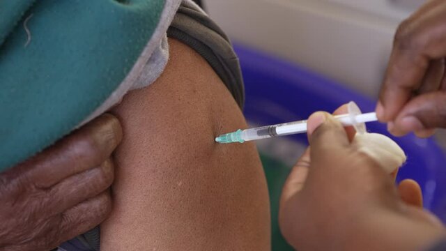 Slow-motion close-up shot of hypodermic syringe needle puncturing the skin of a person when injected with a vaccine shot.