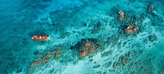Fototapeta na wymiar View from above, stunning aerial view of a wooden boat anchored to some rocks bathed by a crystal clear, turquoise water. Giardinelli island, La Maddalena Archipelago, Sardinia, Italy.