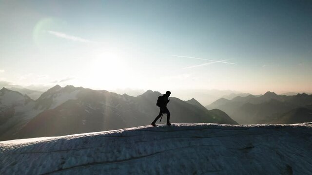 Mountaineer is walking with crampons on the snow and ice covered ridge of a glacier.