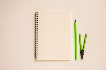 school layout: bright green pencil and compass, beige notebook neatly laid out on a beige background. High quality photo