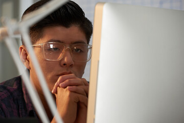Face of pensive young software developer looking at computer screen searching for bugs in...