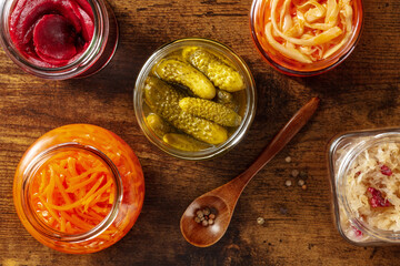 Fermented food, overhead flat lay shot of a variety of pickled vegetables, homemade preserves in mason jars. Healthy vegan ingredients on a wooden table