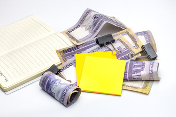 Scattered thousand taka bangladesh banknotes with a notebook, black binder, and sticky notes on white background