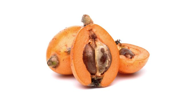 Two halves and one whole loquat rotating on white background.
