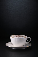 Coffee on black. White cup of cappuccino on a black textured background. Italian cappuccino. Morning coffee in Italy. Close-up on a white cup.