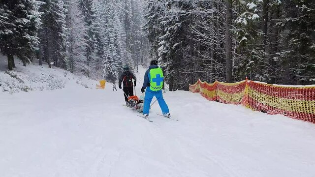 Mountain rescuers transporting an injured skier, going downhill after first aid. Slope rescue, ski patrol service evacuating the victim on a special sledge. Bukovel ski resort, ukraine carpathians.