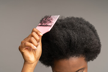 African woman combing curly hair. Cropped image of ethnic female hand holding hairbrush at head...