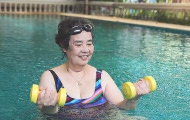 happy and healthy Asian senior woman  working out in the pool with yellow dumbbells. Elderly active lifestyle concept. - obrazy, fototapety, plakaty