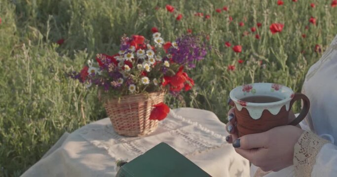Hands hold a cup of tea against the background of a bouquet and a book on the table