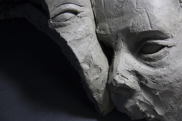Split face. Wet clay sculpture, in the process of creation on black background. Sketched male...