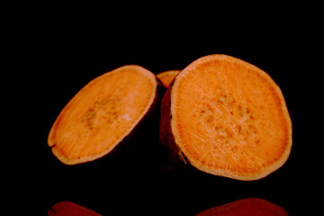 One whole fresh juicy sweet potato cut into several slices, close-up, isolated on black.