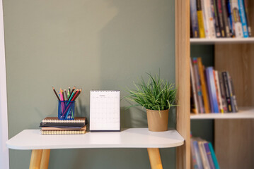 Desk for student education concept. Book, and pencil for study for exam. Calendar and green plant placed on white School table with bookshelf background for student plan to work at home.