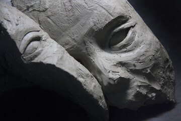 Split male face, in clay, frontal gaze on black background. Sculpture in the modelling stage....