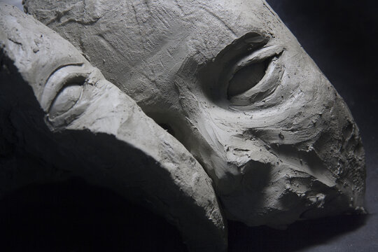 Split male face, in clay, frontal gaze on black background. Sculpture in the modelling stage. Sketched facial features.  