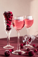 Fototapeta na wymiar set of red berry's alcohol drinks among cranberries scattering on the table, pink gin or vodka infused with cranberry and cherry closeup, elegant minimalism