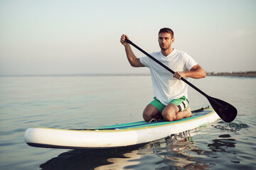 Young man in t-shirt and shorts floating on SUP board
