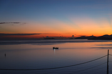 Scenic view from silhouette of fishing boat in calm ocean during sunrise 