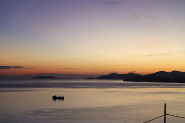 Silhouette of fishing boat sailing on the sea during sunrise with purple and orange sky