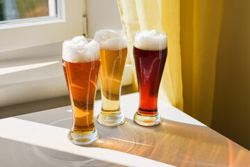 Different sorts of beer in long glasses on table next to window. Natural light at sunny day. Shadows on table. Oktoberfest concept. New normal