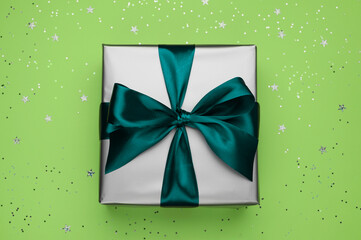 Gift box with bow on green color background with sparkles.