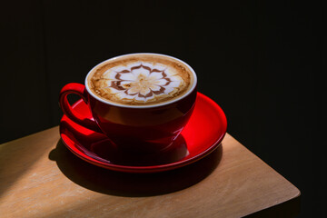 Mocha coffee in a red mug decorated with caramel and chocolate motifs. Place a glass on a wooden floor with a dark shadow background.