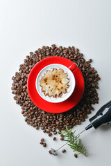 Latte coffee in red mug decorated with caramel and chocolate motifs. Coffee beans are part of the composition.