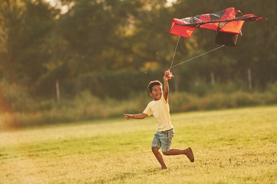 Running with red kite. African american kid have fun in the field at summer daytime