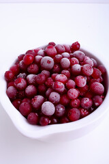 Frozen cranberry in white bowl on white background. Selective focus. Close up of frozen cranberries.