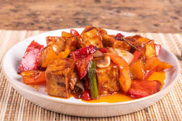 Sweet and sour tofu with peppers and onions in a spicy sauce, portion on a plate, close-up. Korean, Chinese and Japanese cuisine.