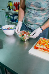 Unrecognizable cook in restaurant kitchen preparing salad to takeaway