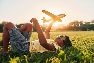 In glasses with toy plane. African american kid have fun in the field at summer daytime