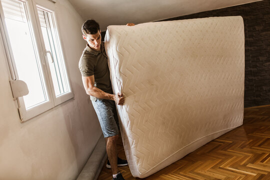 A Man Carries A Mattress While Moving Out Of The Apartment