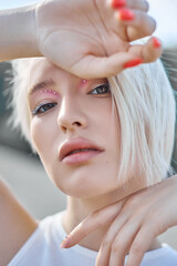 Fototapeta premium Perfect red nail manicure blonde woman short hair. A woman poses in summer in nature on a sunny day