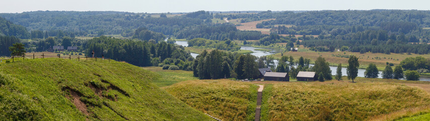 River in the valley. A farm on the horizon. View from the hill to the valley below, the river and the forest. A village far away by the river