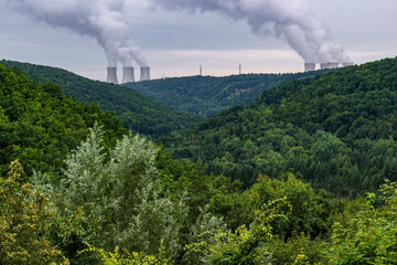 Green valley covered with forest and on the horizon are the cooling towers of a nuclear power plant Dukovany. Contrast of nature and industry. Czech republic.