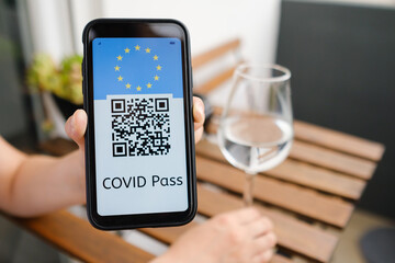 Woman demonstrates Covid pass application or digital health passport with QR code and USA flag in mobile phone sitting in the cafe, 
