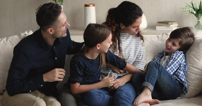 Carefree young parents having fun, playing with cute little children, resting in modern living room. Happy family tickling laughing small kids, entertaining on weekend, enjoying pastime at home.