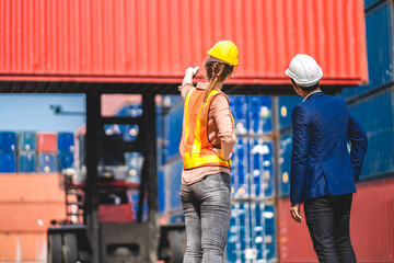 Professional of two engineer container cargo foreman in helmets working standing and using walkie talkie checking stock into container for loading.logistic and business export