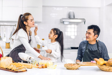 Obraz na płótnie Canvas Portrait of enjoy happy love asian family father and mother with little asian girl daughter child having fun cooking food together with baking cookie and cake ingredient on table in kitchen