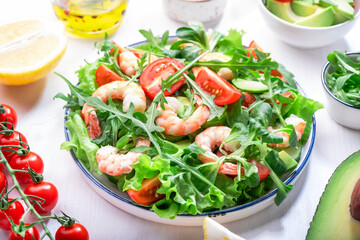 Shrimp salad with cherry tomatoes, arugula, avocado, and oil lemon dressing on white background. Top view