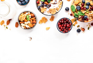 Muesli bowl and organic ingredients for healthy breakfast. Granola, nuts, blueberry, cranberry, oatmeal, greek yoghurt, whole grain flakes on white table