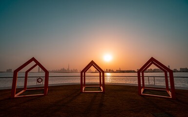 Orange frame houses at the Dubai Creek Harbour waterfront with setting sun and the Dubai skyline in the background at golden hour