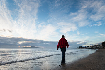 Man walking on the Milford beach at sunrise , North Shore, Auckland