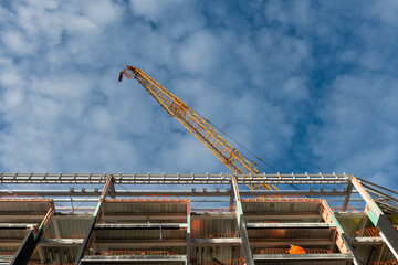 Apartment under construction with orange crane, low angle view. Blue sky with fluffy white clouds.