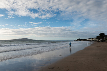 Woman walking on the Milford beach with Rangitoto Island in the distance, North Shore, Auckland