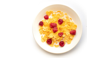 Cornflakes in milk with raspberries on a white plate.